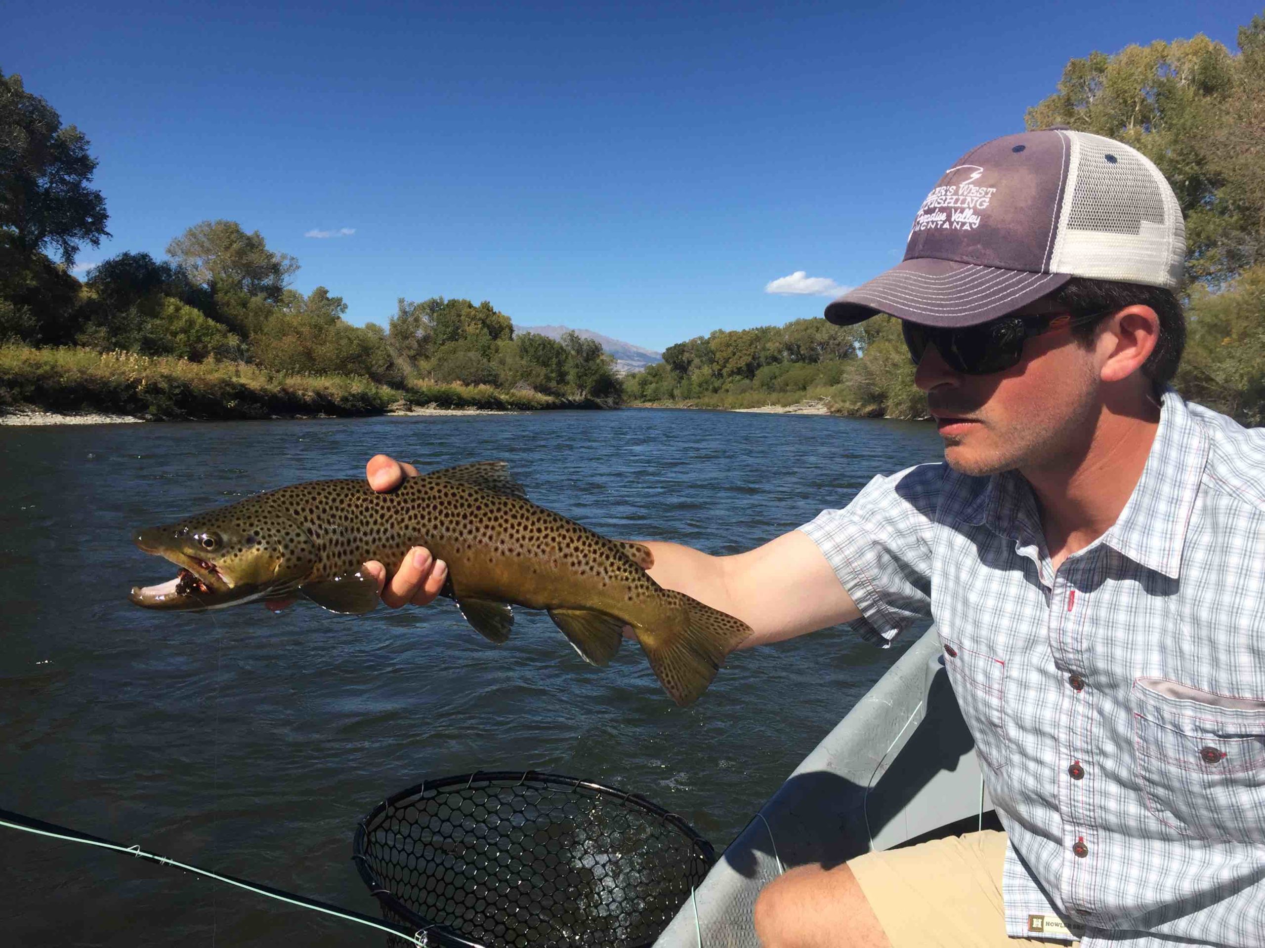 guy holding trout above boat while floating down river